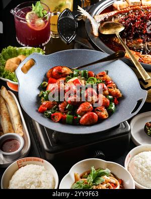 Un festin de fruits de mer dynamique composé d'écrevisses sautées épicées avec des poivrons verts et rouges, sur une table de cuisson animée avec riz et nouilles Banque D'Images