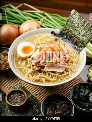 Ramen japonais traditionnel servi dans un riche bouillon avec des œufs durs, des algues et des nouilles ramen. Entouré de garnitures classiques comme le maïs Banque D'Images