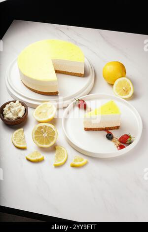 Cheesecake rafraîchissant au citron avec une croûte de biscuit, surmonté d'un glaçage au citron zesté. Une tranche est servie avec des fraises fraîches, des bleuets Banque D'Images
