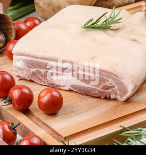 Dalle de poitrine de porc crue fraîche avec peau, garnie de romarin, tomates cerises, piments, sel de mer, et des grains de poivre noir sur papier rustique, idéal Banque D'Images