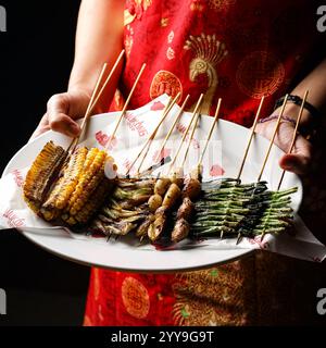 Brochettes de viande grillée épicées servies sur une assiette blanche avec des épices, de l'ail frais, de la soupe et des piments verts, parfaites pour un plat asiatique savoureux Banque D'Images