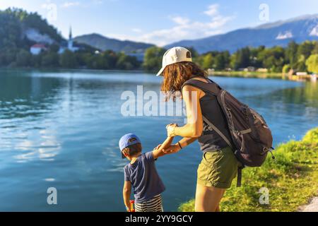 Mère et fils se tenant la main, profitant des vacances d'été au bord de l'eau turquoise du lac saigné, avec l'église emblématique sur l'île saignée en arrière-plan Banque D'Images