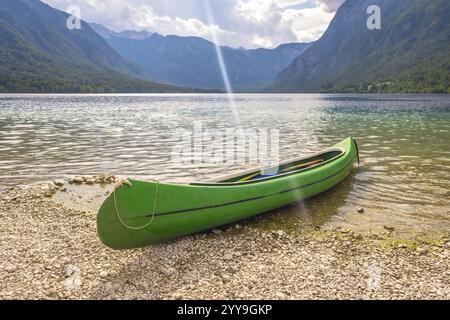 Canot vert reposant sur la rive galbée du lac Bohinj, avec les alpes juliennes en arrière-plan, offrant une vue sereine sur la beauté de la nature Banque D'Images