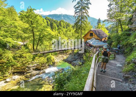 Touristes appréciant la journée d'été à la gorge de vintgar près de Bled en slovénie, marchant sur un chemin près d'un pont en bois et un restaurant avec un beau paysage Banque D'Images