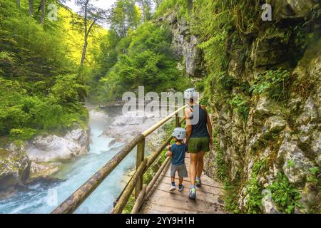 Mère et fils portant des casques marchant sur un chemin en bois et profitant d'une vue imprenable sur la rivière radovna qui coule à travers la gorge de vintgar en slovénie Banque D'Images