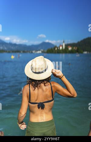 Femme portant un chapeau de soleil regardant le lac Bled île avec église le jour ensoleillé d'été dans les alpes juliennes, slovénie Banque D'Images