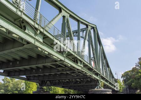 Vue en bas angle d'un pont en acier vert enjambant une rivière, reliant deux côtés avec un ciel bleu clair au-dessus Banque D'Images