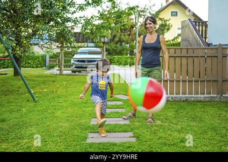 Garçon joyeux jouant avec une balle gonflable avec sa mère dans un jardin d'arrière-cour, profitant du temps de qualité ensemble pendant les vacances d'été Banque D'Images