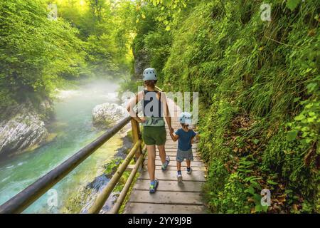 Mère et fils portant des casques marchent sur un sentier en bois le long d'une rivière immaculée, profitant du paysage magnifique de la gorge vintgar près de Bled, s. Banque D'Images