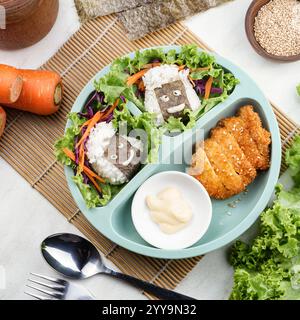 Déjeuner bento mignon et créatif avec boulettes de riz souriantes enveloppées d'algues avec laitue, carottes, chou et poulet pané croustillant Banque D'Images