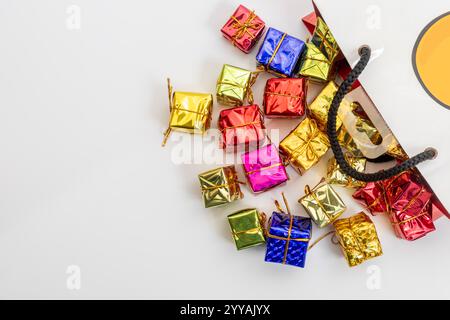 Boîtes-cadeaux miniatures vibrantes de différentes couleurs et rubans d'or débordant d'un sac à provisions élégant, célébrations, fêtes et occasions festives. Banque D'Images