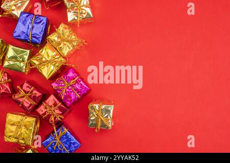 Une vue de dessus de boîtes-cadeaux colorées disposées soigneusement sur un fond rouge, avec un grand espace de copie. Parfait pour les promotions de vacances, salutations festives. Banque D'Images