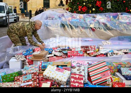 La Valette, Malte. 20 décembre 2024. Un homme protège les cadeaux de Noël de la pluie lors d'un événement caritatif de don de cadeaux de Noël à des enfants dans le besoin à Castille Square à la Valette, Malte, le 20 décembre 2024. Crédit : Jonathan Borg/Xinhua/Alamy Live News Banque D'Images