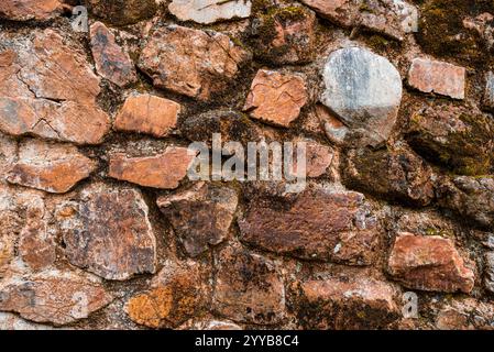 Un mur fait de pierre avec de la mousse poussant dessus. Le mur est fait de nombreuses pierres de tailles différentes Banque D'Images