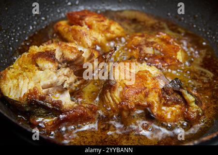 gros plan de morceaux de poisson assaisonnés ou marinés frits dans de l'huile de noix de coco, poisson croustillant brun doré avec de l'huile bouillonnante et brillante, angle de côté Banque D'Images