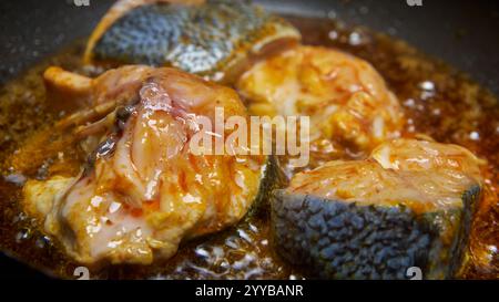 gros plan de morceaux de poisson assaisonnés ou marinés frits dans de l'huile de noix de coco, poisson croustillant brun doré avec de l'huile bouillonnante et brillante, angle de côté Banque D'Images