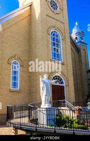 Une statue blanche d'un homme tenant une croix se trouve à l'extérieur d'une église. La statue est entourée d'une clôture métallique Banque D'Images