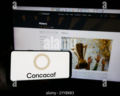 Dans cette illustration photo, une personne tient un smartphone avec le logo de l'association de football CONCACAF en face du site. Banque D'Images