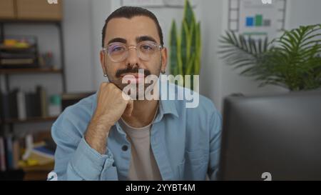 Homme hispanique avec moustache et lunettes dans un bureau intérieur, regardant avec confiance la caméra. Banque D'Images