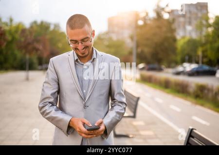Portrait d'homme d'affaires heureux qui est la messagerie au téléphone. Jeune homme d'affaires debout dans la rue et à l'aide d'un smartphone. Banque D'Images