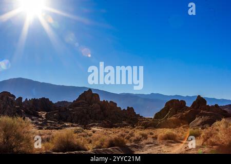 Le soleil brille sur un paysage désertique rocheux. Le ciel est d'un bleu profond, et les montagnes au loin sont couvertes de neige. La scène est p. Banque D'Images