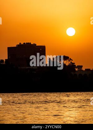 Beau coucher de soleil sur le Nil au Caire, Egypte, vu d'un bateau avec des silhouettes de bâtiment en arrière-plan Banque D'Images