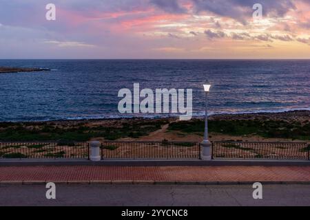 La vue sur la côte offre un coucher de soleil doux, des lampadaires lumineux et une ambiance sereine en bord de mer. Il est idéal pour transporter la tranquillité, la beauté côtière, Banque D'Images