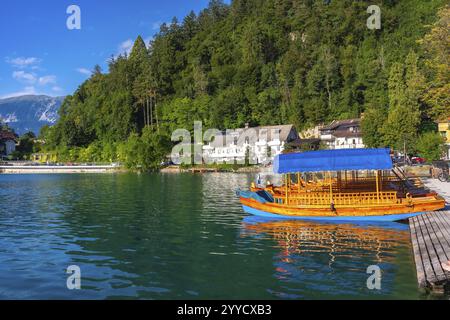 Bateau de pletna traditionnel en bois avec un auvent bleu amarré sur le lac pittoresque saigné, encadré par les superbes alpes juliennes Banque D'Images