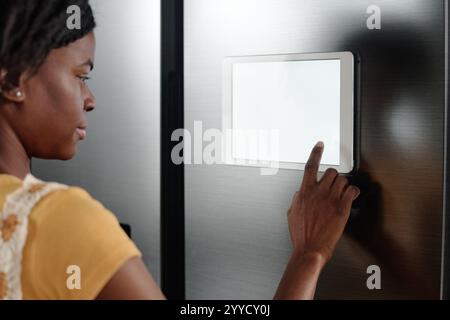 Photo sur l'épaule d'une femme afro-américaine utilisant une tablette sur la porte du réfrigérateur pour régler le réfrigérateur intelligent Banque D'Images