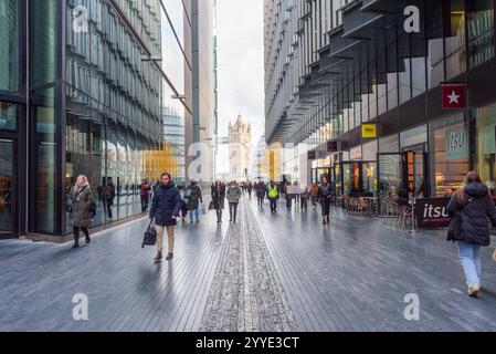 Londres, Royaume-Uni - 3 décembre 2024 : les gens marchent le long d'une passerelle à travers des immeubles de bureaux modernes à Londond Bridge City. Tower Bridge est en arrière-plan. Banque D'Images