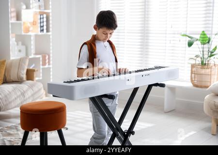 Garçon mignon jouant synthétiseur à la maison. Instrument de musique électronique Banque D'Images