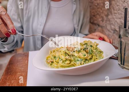 Femme dégustant une assiette de pâtes au pesto, au poulet et au parmesan, déjeunant dans un restaurant Banque D'Images