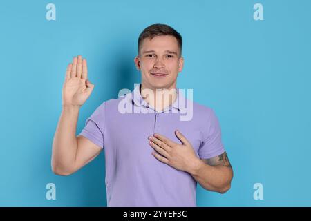 Homme faisant promesse avec la main levée sur fond bleu clair. Geste de serment Banque D'Images