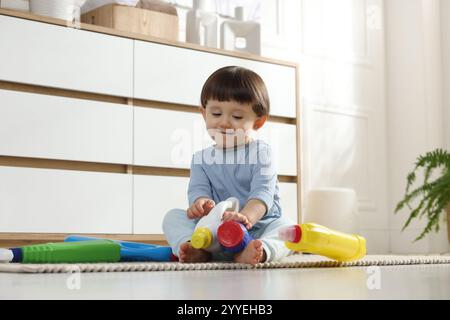 Petit garçon jouant avec des bouteilles de détergents près de l'armoire à la maison. Enfant en danger Banque D'Images