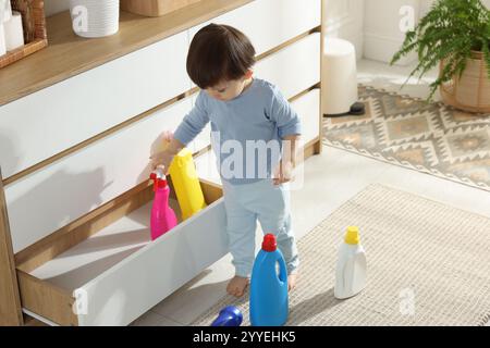 Petit garçon jouant avec des bouteilles de détergents près de l'armoire à la maison. Enfant en danger Banque D'Images