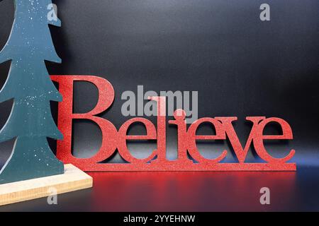 Le mot croire à côté d'un arbre de Noël sculpté avec un fond noir sans couture propre Banque D'Images