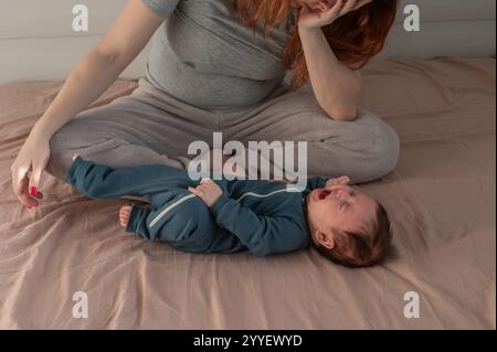Une femme caucasienne est assise sur un lit à côté d'un bébé qui pleure. Dépression du post-partum. Banque D'Images