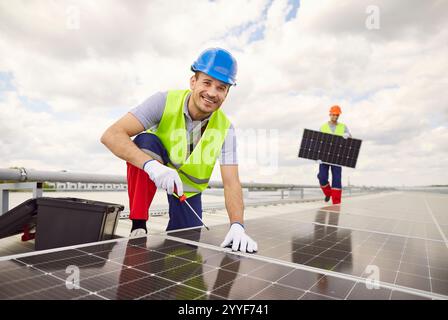Portrait de travailleur souriant installant ou entretenant des panneaux solaires sur le toit Banque D'Images