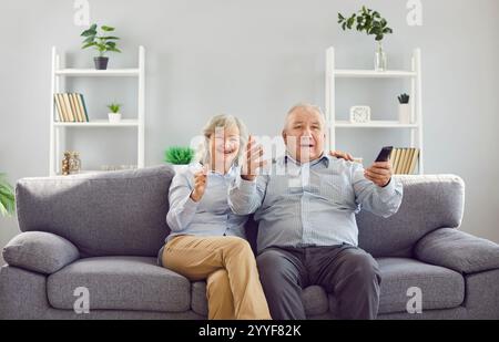 Couple senior regardant le football à la télévision tenant la télécommande de la télévision et soutenant l'équipe sportive ensemble. Banque D'Images