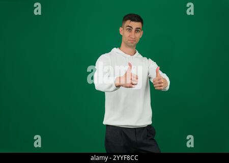 Jeune homme indien portant un sweat-shirt violet debout sur un signe de succès de fond rose isolé faisant un geste positif avec la main, les pouces vers le haut souriant et heureux. Expression joyeuse et gagnant Banque D'Images