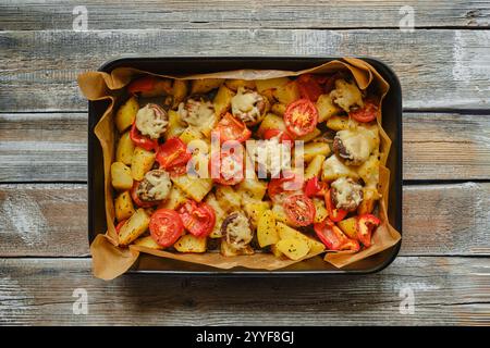 Vue aérienne de pommes de terre rôties, champignons et tomates garnis de fromage fondu, disposés sur une plaque de cuisson sur une table rustique en bois Banque D'Images