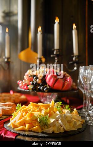 Un plateau de fromages magnifiquement arrangé présente un assortiment de fromages ainsi qu'un étalage de fruits coloré. Des bougies élégantes illuminent la table, créa Banque D'Images
