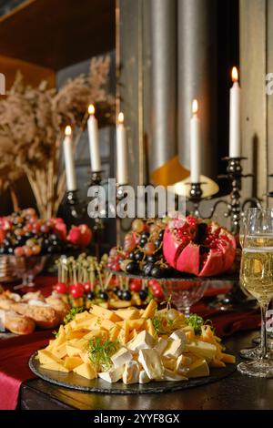 Une table à manger magnifiquement agencée dispose d'un assortiment de fromages, de fruits frais et de bougies élégantes, créant une atmosphère chaleureuse et accueillante pour Banque D'Images