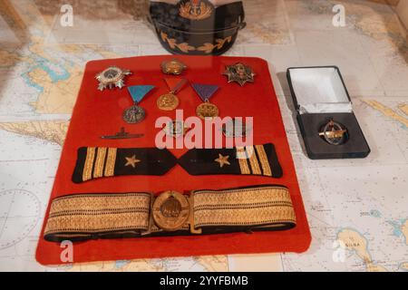 26 octobre 2024, Tivat, Monténégro : collection d'accessoires, médailles et insignes de capitaine de marine affichés sur tissu rouge avec fond de cartes nautiques Banque D'Images