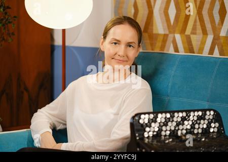 Dans un salon chaleureusement décoré, une femme d'âge moyen s'assoit confortablement sur un canapé bleu, souriant doucement. Banque D'Images