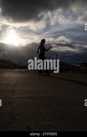 Silhouette d'une jeune fille grecque pratiquer le skateboard dans le port de la ville de Naoussa sur l'île de Paros dans l'archipel des Cyclades en Grèce sur 1 Banque D'Images