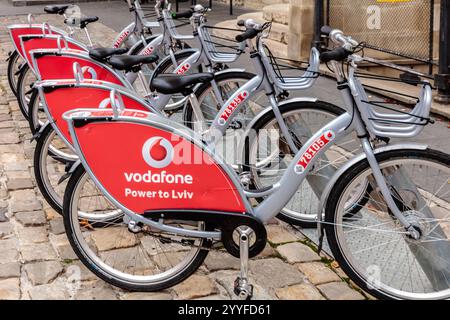 Une rangée de vélos avec des publicités rouges et argentées pour Vodafone. Les vélos sont garés dans une rue pavée Banque D'Images