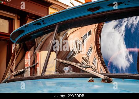 Une voiture bleue avec un pare-brise sale et un reflet d'un bâtiment dans le rétroviseur. La scène est quelque peu mélancolique Banque D'Images