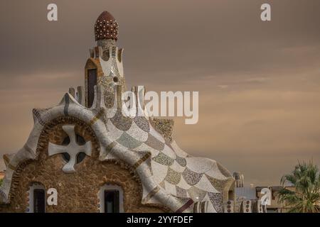 Bâtiment emblématique conçu par Gaudí dans le parc Güell, Barcelone, présentant des détails complexes en mosaïque sous un ciel couvert d'humeur sombre Banque D'Images