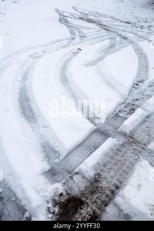 Traces de pneu de voiture courbant sur une route couverte de neige et de glace en hiver Banque D'Images